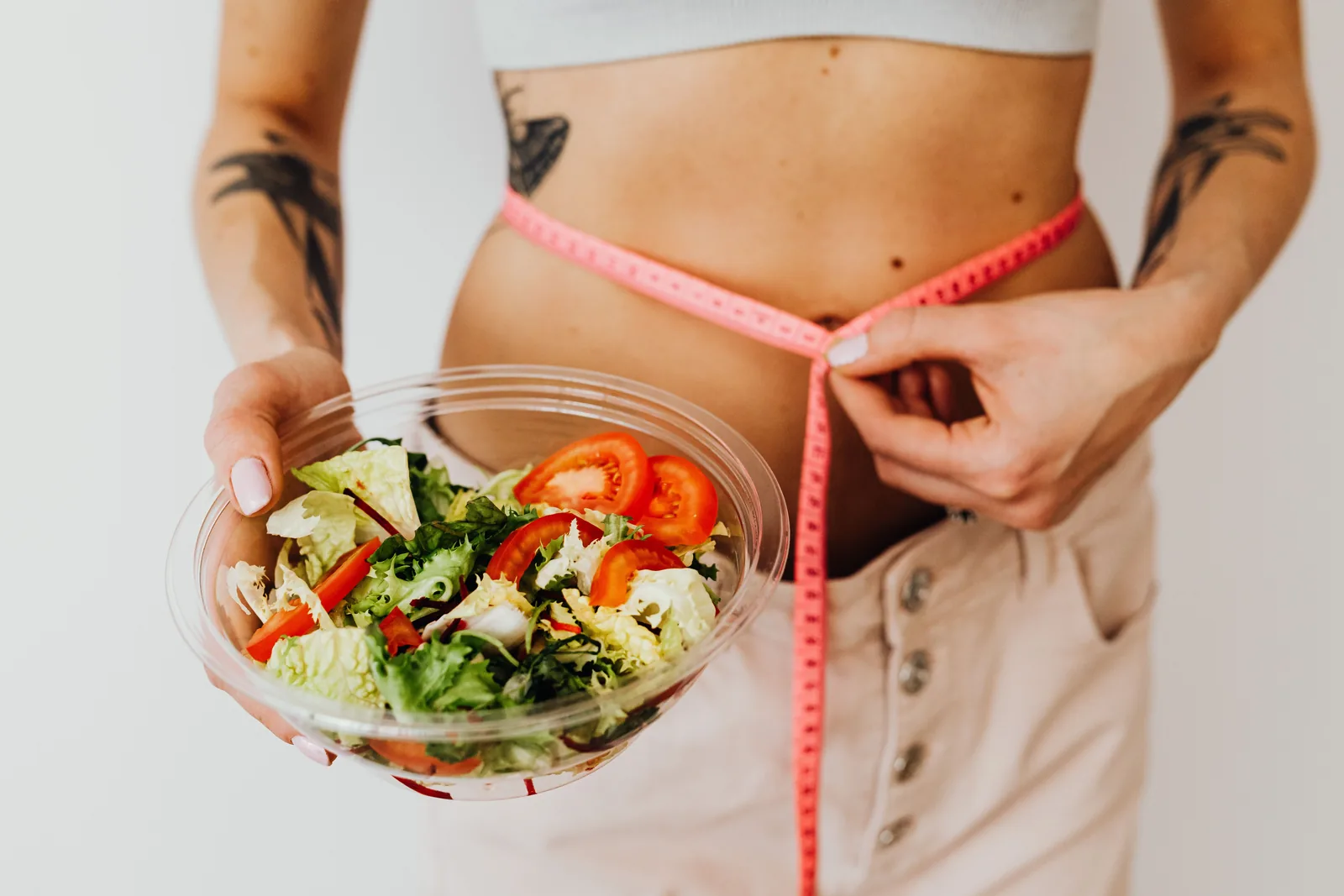 Holding a bowl of salad while measuring the waist