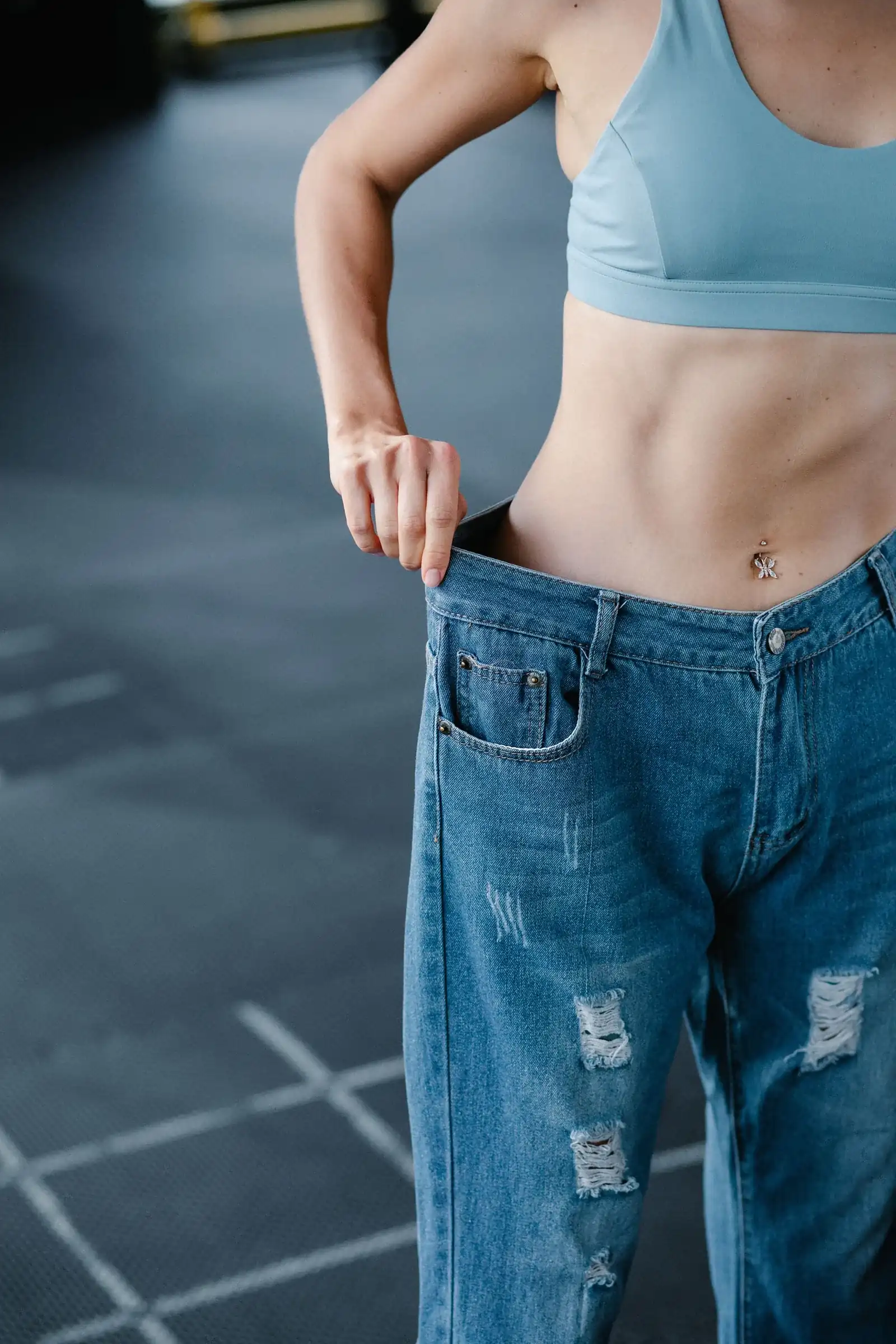 Loose jeans held at the waist in a gym