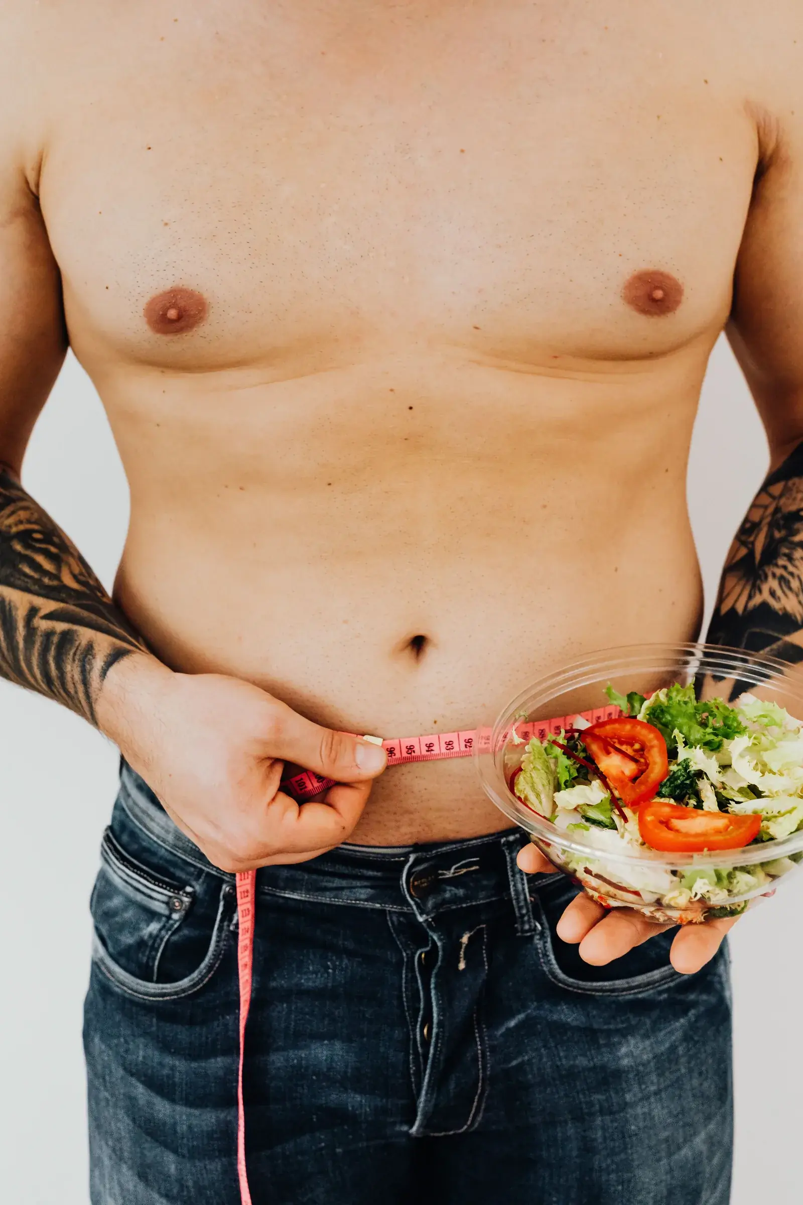 A man measuring his waist while holding a bowl of salad