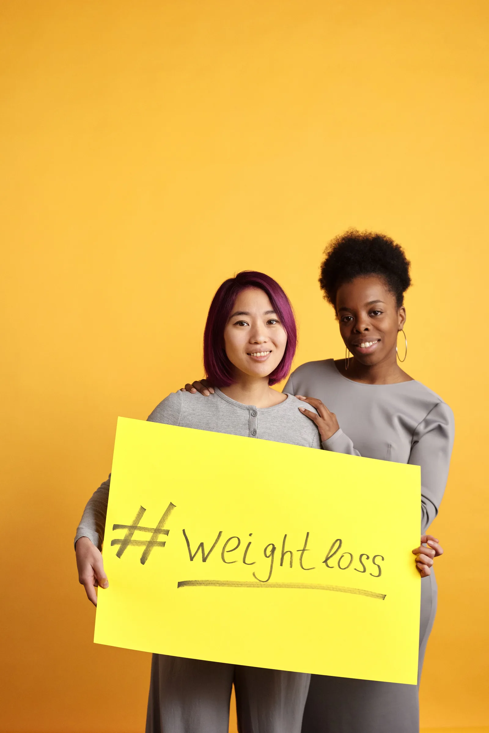 Two people holding a weight loss sign